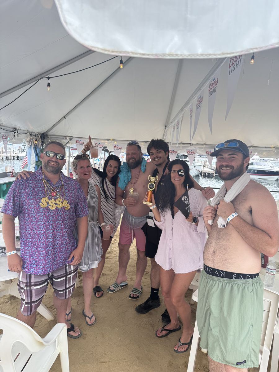 Friends in pirate gear holding a trophy under a beach tent